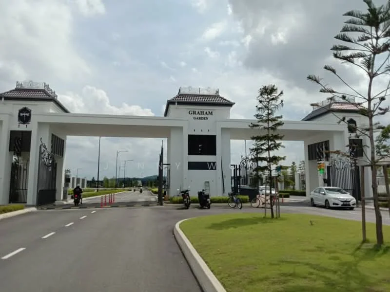 Exterior type: main entrance gate; features: white painted facade, tall entrance pillars, gated entry, landscaped green lawn, paved driveway, security guard house, decorative lighting, signage with 'Graham Garden', surrounding palm trees, open road access; style: modern.