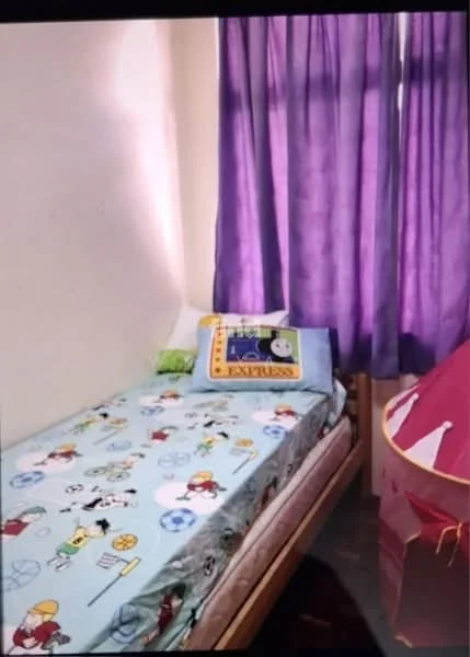 Bedroom features: single bed with colorful bedding, purple curtains, wall with light-colored paint, pillow with cartoon design, green decorative pillow, tent play structure, wooden bed frame, flooring with dark finish.