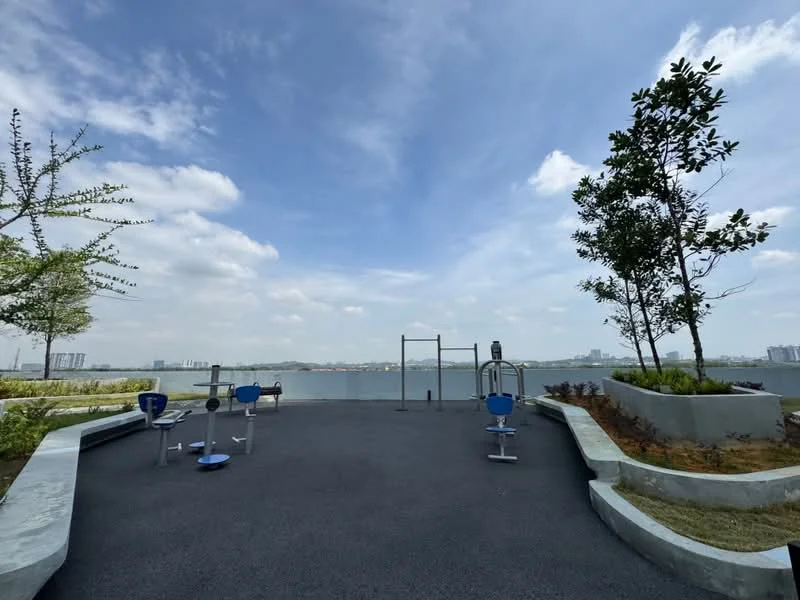 Exterior type: landscape garden; features: outdoor gym equipment, paved walkway, manicured landscaping, planter boxes with shrubs, view of water body, city skyline in background, open space, trees, blue sky; style: modern.