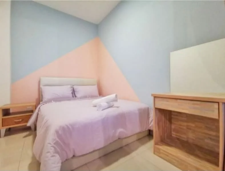 Bedroom features: queen-size bed with upholstered headboard, light purple bedding, wooden bedside table with drawer, wooden desk, painted walls in light blue and peach, tile flooring, window with no visible treatment, rolled towels on the bed; style: modern.