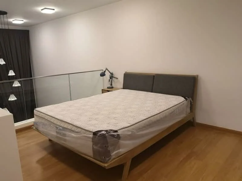 Bedroom features: queen-size bed with mattress protector, wooden bed frame, nightstand with lamp, laminate flooring, white painted walls, glass railing, ceiling light fixtures, dark curtains; style: modern.