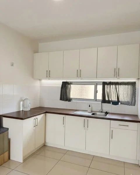 Kitchen features: white cabinetry, brown laminate countertop, single-bowl stainless-steel sink, chrome pull-down faucet, white tiled backsplash, floor-to-ceiling window, grey sheer curtains, ceramic tile flooring, built-in cabinets, under-cabinet lighting; style: modern.