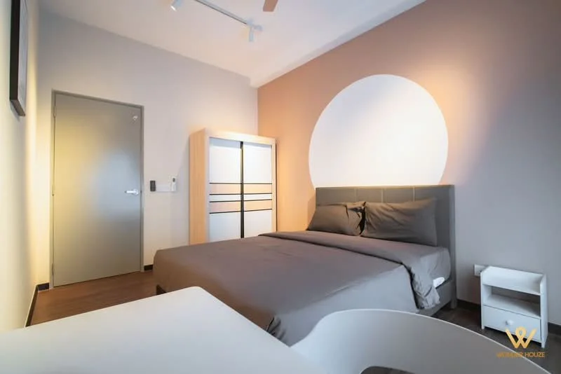 Bedroom features: king-size bed with grey bedding, upholstered headboard, white bedside table, built-in wardrobe with sliding doors, light wood flooring, cream painted walls, accent wall with circular design, ceiling fan, wall-mounted light fixture, window with no visible treatment; style: modern.