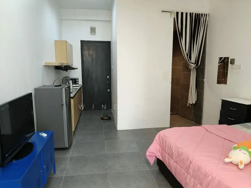 Room features: grey tile flooring, white painted walls, black door, kitchenette with wooden cabinets, stainless-steel fridge, microwave, kitchen countertop, wall-mounted TV, bed with pink bedding, decorative stuffed toy on bed, black bedside table, mirror on wall, striped curtain, shower area visible in background; style: modern.