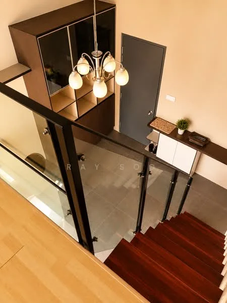 Room features: wooden staircase, glass railing, chandelier with multiple bulbs, dark wood cabinetry, light-colored walls, grey tiled flooring, console table with drawers, decorative plant on console table, door with modern handle; style: modern; view: staircase.