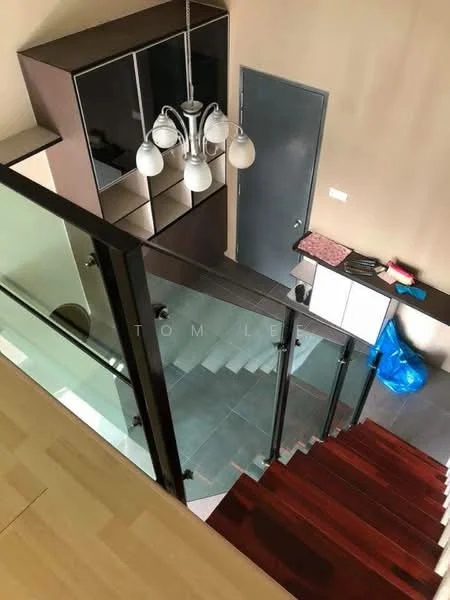 Room features: wooden staircase, glass railing, dark wood flooring, light-colored walls, modern chandelier with multiple bulbs, built-in cabinetry with black and wood finish, grey door, countertop with pink surface, blue plastic bag; style: modern; view: staircase.