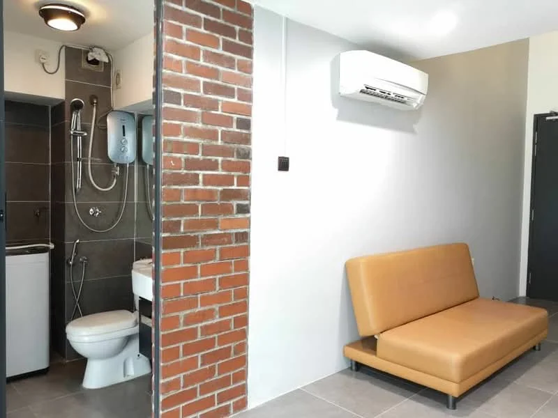 Bathroom features: exposed brick wall, grey ceramic tile flooring, white toilet, chrome showerhead, wall-mounted shower, white sink with cabinet, washing machine, wall-mounted water heater, recessed ceiling light, air conditioning unit; style: modern. Living features: brown leather sofa, grey tile flooring, white painted walls, recessed ceiling light, air conditioning unit; style: modern.