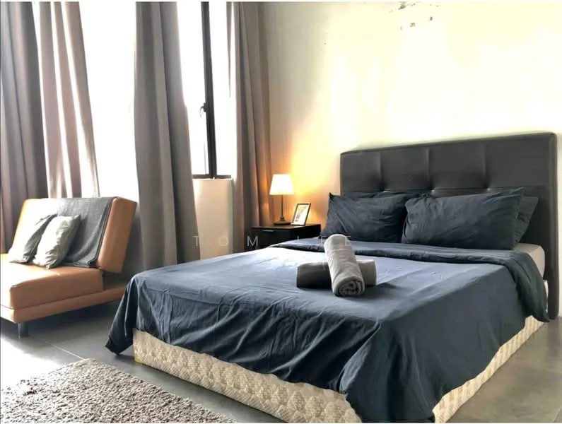 Bedroom features: king-size bed with dark blue bedding, upholstered headboard in dark grey, two grey towels on the bed, bedside lamp with warm light, floor-to-ceiling window with sheer curtains, grey area rug, sofa chair in orange fabric, decorative pillows on sofa, plain painted walls in light colour, concrete flooring; style: modern.