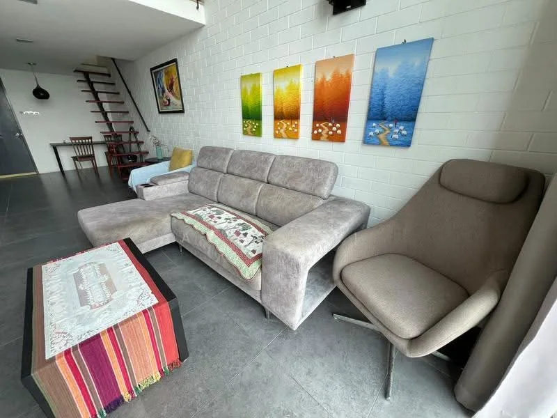 Living features: grey fabric sectional sofa, beige armchair, coffee table with colorful textile runner, framed artwork on wall, white painted walls, dark tile flooring, decorative throw blanket on sofa, wooden dining table visible in background, staircase in background; style: modern.