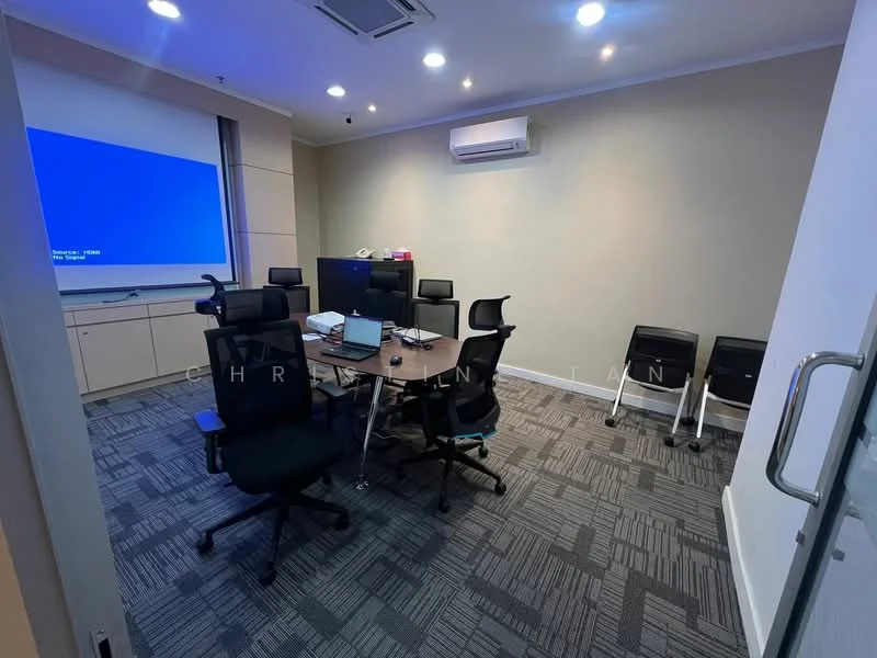 Room features: conference table, black office chairs, projector screen, wall-mounted projector, air conditioning unit, grey painted walls, carpet flooring with geometric pattern, glass door, two exercise bikes; style: modern.