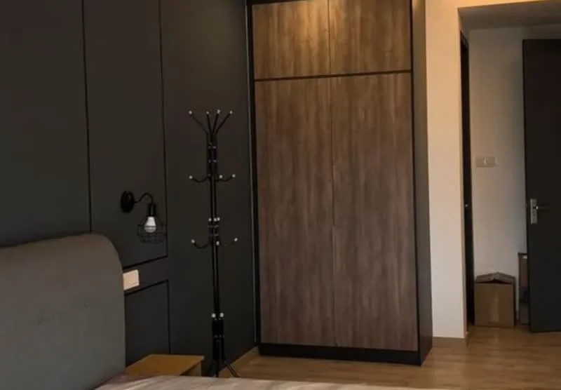 Bedroom features: grey upholstered bed, wooden flooring, dark accent wall, built-in wardrobe with wood finish, wall-mounted reading light, coat rack, neutral bedding, decorative wall paneling; style: modern.