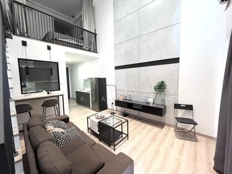 Living features: sofa in brown fabric, coffee table with black metal frame, TV console in black, wall-mounted TV, decorative plant, wooden flooring, high ceiling, large wall with concrete finish, open staircase, bar stools at kitchen counter, pendant lighting, curtains in grey, area rug with geometric pattern; style: modern. Kitchen features: kitchen counter with bar stools, black cabinetry, open shelving, stainless-steel appliances, sink, backsplash with tile finish; style: modern.