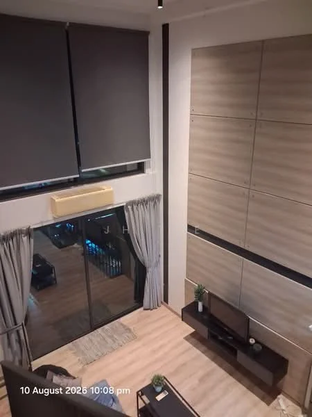 Living features: floor-to-ceiling windows, grey roller blinds, wooden flooring, wall-mounted TV, black TV console, decorative plant on console, light grey curtains, air conditioning unit, area rug, sofa, coffee table; style: modern; view: city.