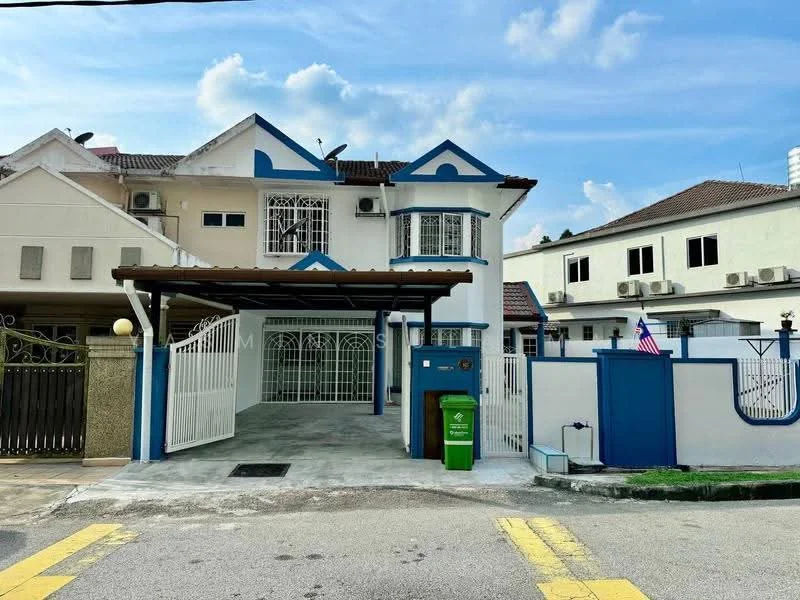 Exterior type: semi-detached house; features: white painted facade, blue accents on windows and roof, gated entrance with white metal gate, car porch with awning, manicured lawn, paved driveway, visible air conditioning units, surrounded by residential buildings, flagpole with Malaysian flag, decorative wall with blue trim; style: modern.