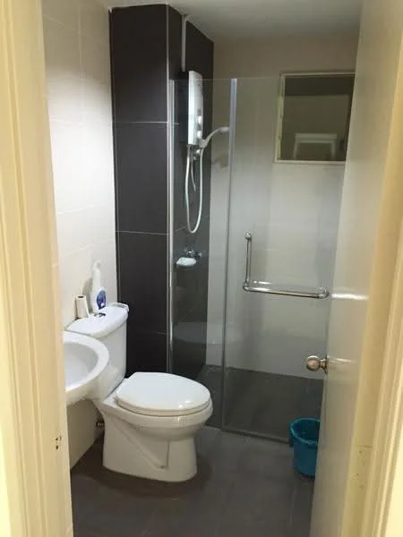 Bathroom features: white ceramic toilet, glass shower enclosure, chrome shower head, wall-mounted shower mixer, dark grey tiled walls, light grey tiled flooring, white sink, mirror above sink, grab bar, blue plastic waste bin; style: modern.