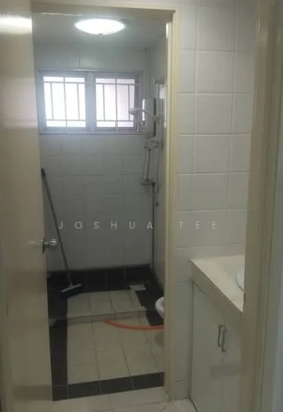 Bathroom features: white tiled walls, black tiled flooring, shower area with handheld shower, toilet, single-sink vanity with cabinet, mirror above sink, window for natural light, shower curtain rod, cleaning tool visible.