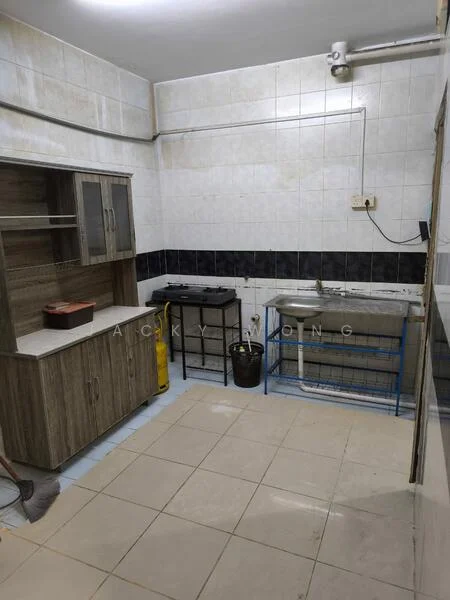 Kitchen features: white tiled walls, grey tiled backsplash, light grey floor tiles, wooden cabinetry with laminate finish, countertop with laminate surface, stainless-steel sink, single-bowl sink, gas stove, exposed plumbing, open shelving, bucket for storage, cleaning supplies visible.