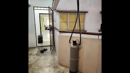 Room features: concrete flooring, white painted walls, wooden railing, doorway leading to another room, hanging gas cylinder, slippers on the floor.