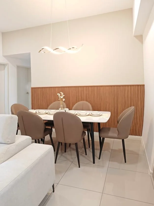 Dining features: 6-seater dining table, marble-top dining table, upholstered dining chairs in beige, wood panel accent wall, pendant light fixture, neutral wall colour, glossy tile flooring, decorative vase on table; style: modern.