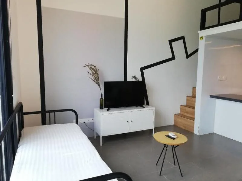 Living features: single bed with white bedding, black metal bed frame, white TV console, flat-screen TV, small round coffee table, grey tiled flooring, decorative plant in vase, staircase with wooden steps, geometric wall design in black and grey, wall-mounted lighting; style: modern.