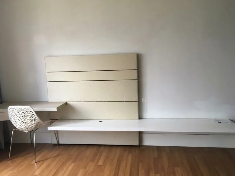 Room features: light wood flooring, plain white walls, built-in wall panel with horizontal lines, white desk with integrated storage, transparent chair with decorative pattern, minimalist design, no visible window treatments; style: modern.
