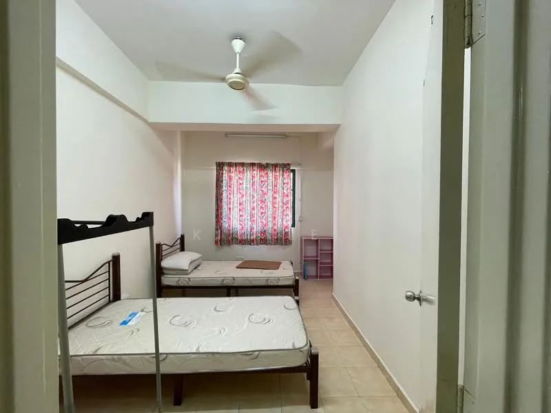 Bedroom features: two single beds with metal frames, mattresses on both beds, ceiling fan, window with floral curtains, light-colored walls, tiled flooring, small pink shelving unit, wooden door, neutral-colored bedding.