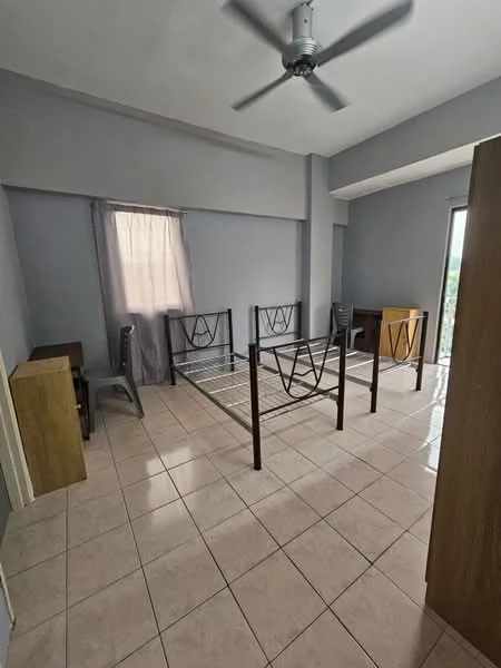 Bedroom features: light grey painted walls, tiled flooring, 5-blade ceiling fan, window with sheer curtains, metal bed frame without mattress, two wooden bedside tables, one plastic chair, one wooden chair, door leading outside.