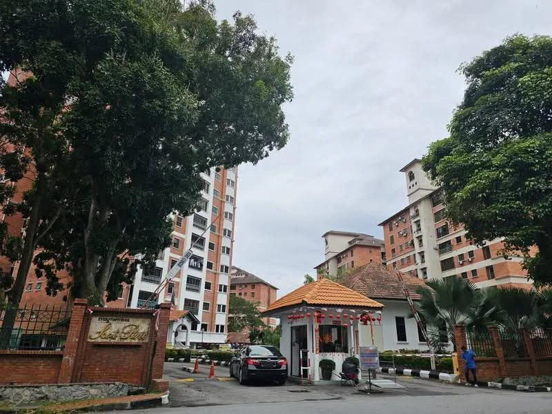 Exterior type: low-rise apartment block; features: brick facade, gated entrance, guard house at entrance, landscaped garden, mature trees, paved driveway, signage at entrance, surrounded by greenery; style: modern.