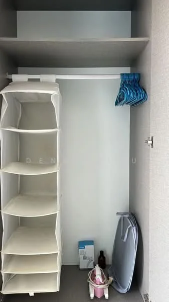 Room features: built-in shelving unit, hanging rod for clothes, blue plastic hangers, storage bins, grey ironing board, cleaning supplies, neutral wall colour, grey flooring; style: minimalist.