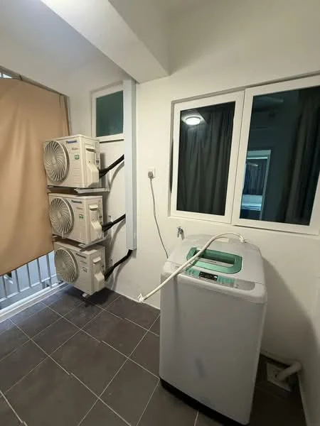 Laundry features: front-load washing machine, 3 wall-mounted split AC units, grey tiled flooring, white painted walls, window with white frame, curtain for privacy, drainage outlet, light fixture on ceiling.