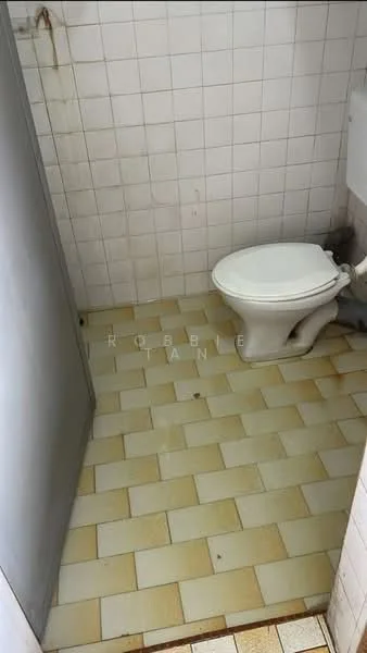 Bathroom features: white toilet, white tiled walls, beige and white patterned floor tiles, metal partition, visible plumbing, stains on wall, small space layout.