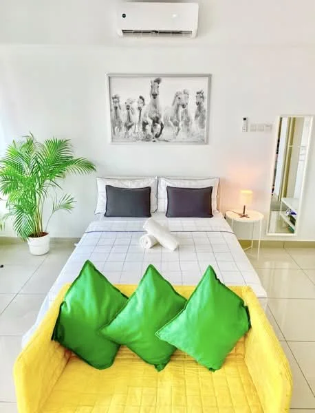 Bedroom features: queen-size bed with white bedding, two grey accent pillows, white bed frame, white walls, tile flooring, wall-mounted split AC, framed artwork with animal print, green potted plant, small white side table, table lamp, yellow sofa with green cushions, mirror on the wall; style: modern.