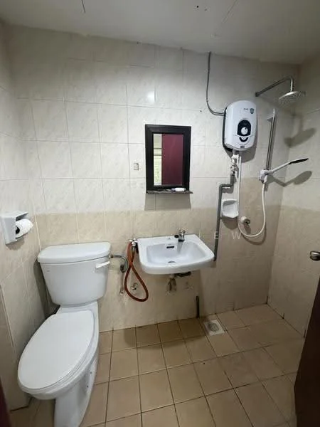 Bathroom features: white ceramic toilet, single-sink vanity with wall-mounted faucet, mirror above sink, shower with handheld showerhead, water heater mounted on wall, beige tiled walls, light beige floor tiles, grab bar next to shower, toilet paper holder, wall-mounted soap dispenser.