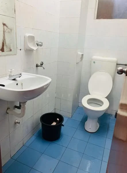 Bathroom features: white ceramic toilet, single-sink vanity with chrome faucet, blue ceramic tile flooring, white tiled walls, mirror above sink, hand soap dispenser, bucket on floor.