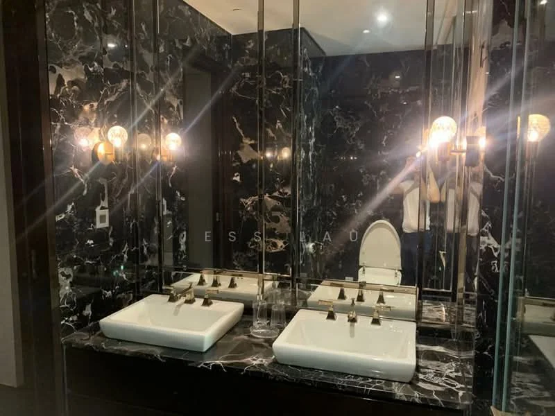 Bathroom features: black marble walls, black marble flooring, double-sink vanity with square basins, gold faucets, backlit mirrors, wall-mounted lighting fixtures, one-piece toilet, dark wood cabinetry; style: luxury.