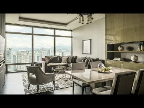Living features: floor-to-ceiling windows, grey fabric sectional sofa, accent chairs in light grey, round coffee table with metallic base, area rug with geometric pattern, wall-mounted TV, built-in shelving with decorative items, recessed downlights, decorative wall art, dark wood flooring; style: modern; view: city.