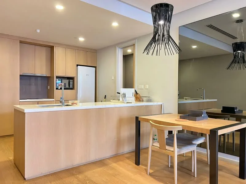 Kitchen features: light wood cabinetry, white quartz countertop, stainless-steel sink, chrome pull-down faucet, built-in oven, freestanding fridge, pendant light fixture, open shelving, wooden dining table, upholstered dining chair, mirror on wall, wooden flooring; style: modern.