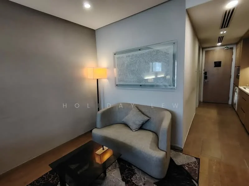 Living features: curved grey fabric sofa, glass coffee table, area rug with geometric pattern, framed artwork on wall, wooden flooring, recessed ceiling lights, wall-mounted light fixture, neutral painted walls; style: modern. Room features: wooden cabinetry, doorway leading to hallway, light switch visible.