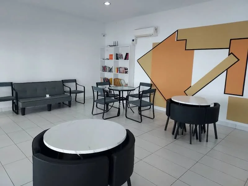 Room features: white painted walls, grey accent wall, tile flooring, ceiling lights, black metal chairs, round white dining tables, grey fabric sofa, bookshelf with books, decorative wall art; style: modern.