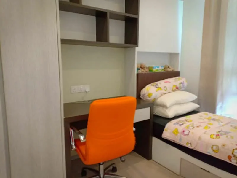 Bedroom features: single bed with bedding, orange office chair, wooden desk, built-in shelving unit, light-colored walls, neutral flooring, decorative stuffed toys, pillow with cartoon pattern; style: modern.