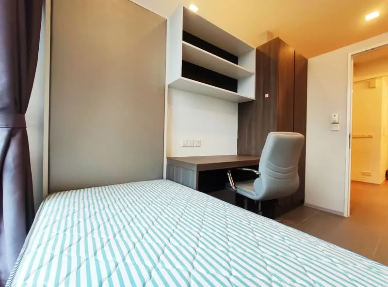 Bedroom features: single bed with mattress, built-in desk, ergonomic office chair, wood cabinetry, shelves above desk, grey accent wall, curtains, flooring with tile finish, light fixture on ceiling; style: modern.