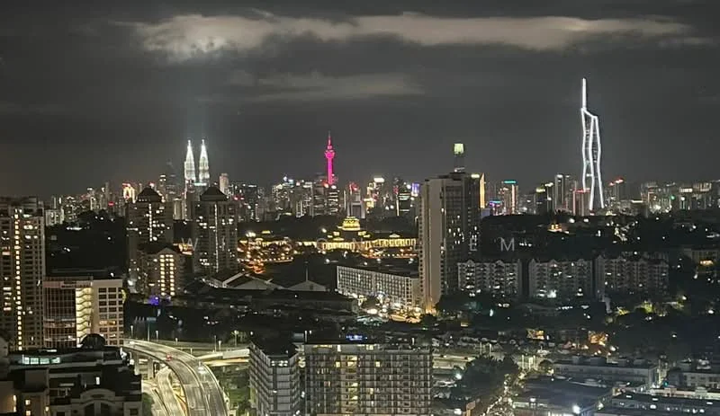 Exterior type: high-rise condominium; features: city skyline view, night lighting, urban landscape, multiple high-rise buildings, prominent landmarks visible, surrounded by greenery; style: modern.