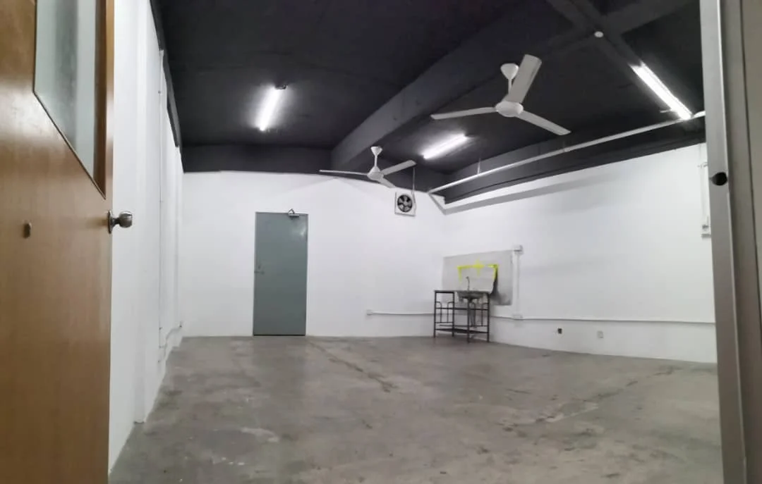 Room features: concrete flooring, white painted walls, black painted ceiling, 2 ceiling fans, 1 wall-mounted air conditioning unit, 1 grey door, 1 grey door with window, whiteboard, exposed ductwork, fluorescent lighting; style: industrial.