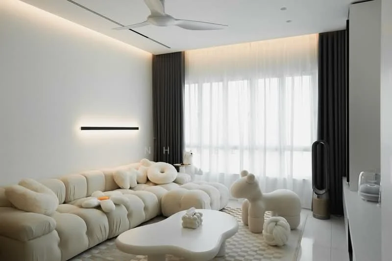 Living features: L-shape sectional sofa in cream, decorative cushions in various shapes, white coffee table with organic shape, floor-to-ceiling windows with sheer curtains, dark grey curtains, ceiling fan, wall-mounted light fixture, decorative plush animal, area rug with geometric pattern, minimalist decor, white walls, polished tile flooring; style: modern.