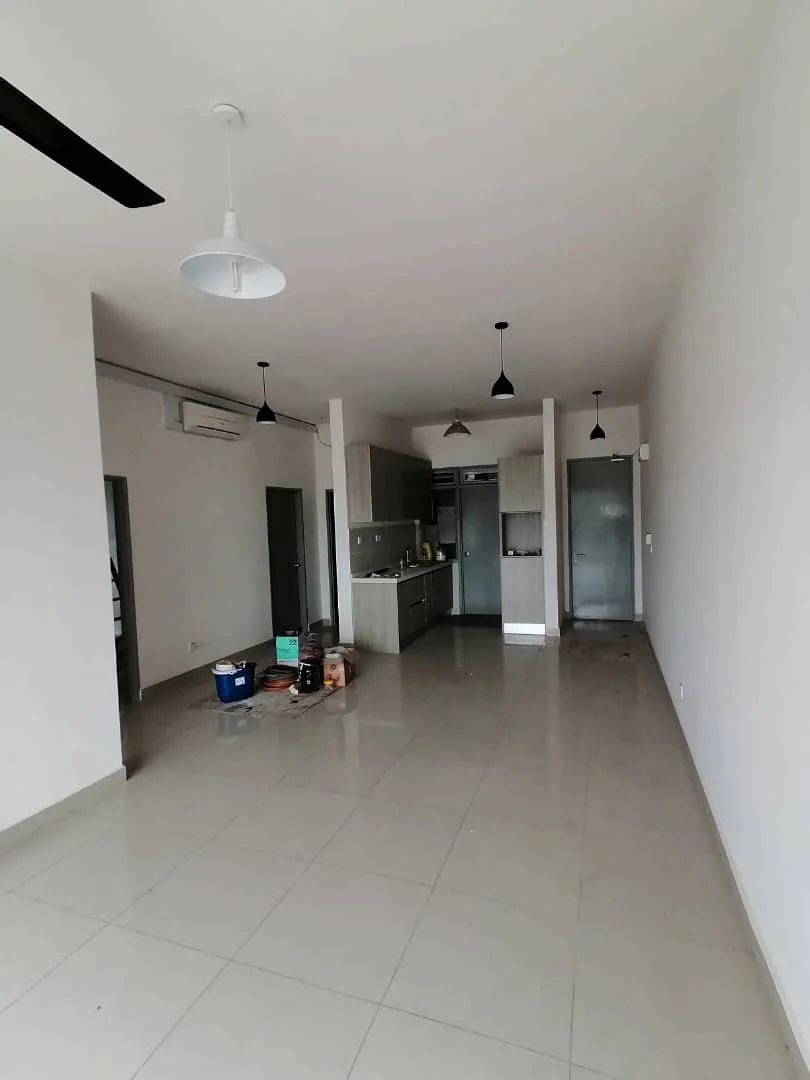 Living features: white painted walls, large glossy beige ceramic tile flooring, high ceiling, recessed ceiling area, black ceiling fan, white pendant light, wall-mounted split air conditioner, open-plan layout, sliding glass door opening to adjacent space, plain white ceiling, minimalist interior, unfurnished floor space; style: minimalist. Kitchen features: light wood and dark grey cabinetry, laminate countertop, grey tile backsplash, compact galley kitchen, single-bowl stainless-steel sink, chrome faucet, built-in oven niche, stainless-steel refrigerator, upper cabinets, lower cabinets, pendant light above kitchen area, tiled kitchen floor continuing from living area; style: modern. Hallway features: white painted walls, glossy beige ceramic tile flooring, multiple doorways, grey metal door, narrow circulation space, plain ceiling, black pendant lights; style: minimalist.
