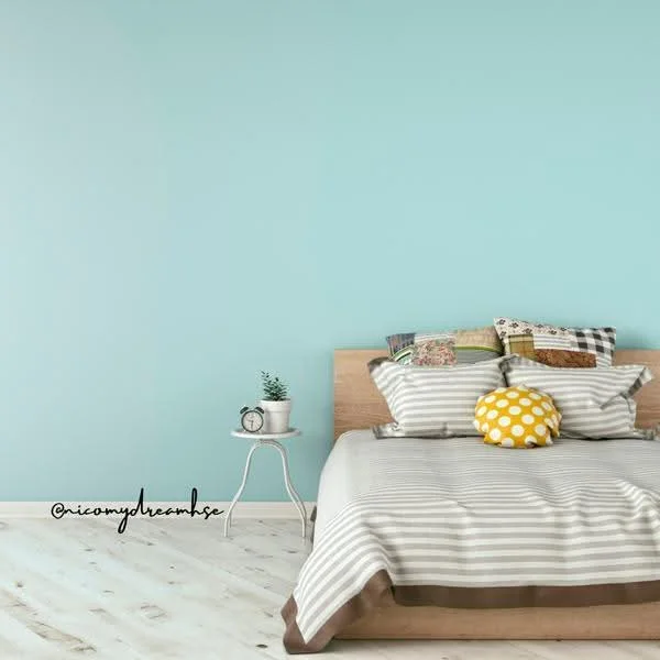 Bedroom features: light blue painted walls, wooden bed frame, striped bedding in grey and white, decorative pillows with various patterns, yellow polka dot pillow, white bedside table, wooden flooring, small potted plant on bedside table; style: modern.