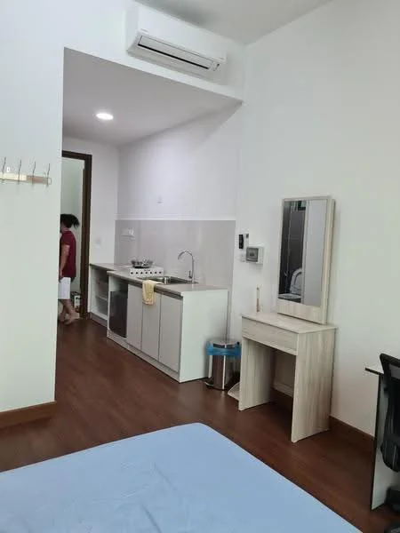 Room features: wooden flooring, white painted walls, kitchenette with cabinets, stainless-steel sink, built-in stove, countertop, mirror on desk, desk with chair, wall-mounted air conditioning unit, light fixture, clothes hook, trash bin; style: modern.