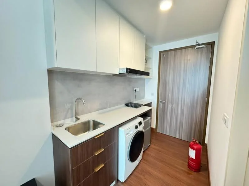 Laundry features: white upper cabinets, brown lower cabinets, white countertop, stainless-steel sink, built-in washing machine, front-load dryer, fire extinguisher, wooden flooring, light fixture, grey wall, door with handle; style: modern.