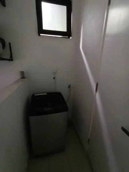 Laundry features: top-load washing machine in silver, white painted walls, tile flooring, small window, shelf above washing machine, door leading out.