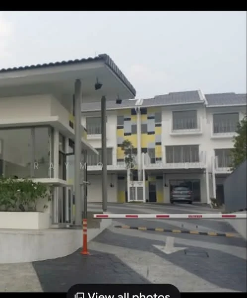 Exterior type: linked terrace house; features: modern facade with yellow and blue accents, two-storey building, gated entrance with security barrier, paved driveway, landscaped area with plants, multiple parking spaces, roof with grey tiles, windows with white frames, visible car parked, surrounded by greenery; style: modern.